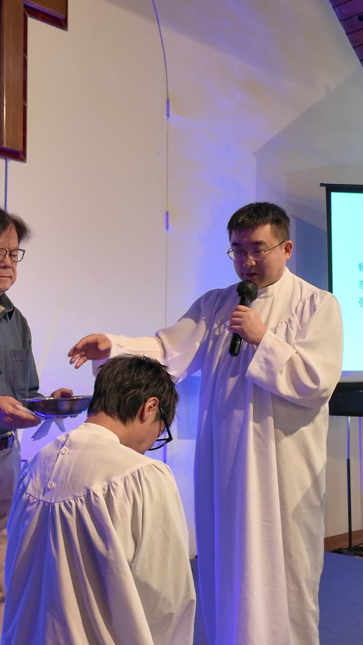 牧师穿着白袍,按手为低头的受洗者施洗
