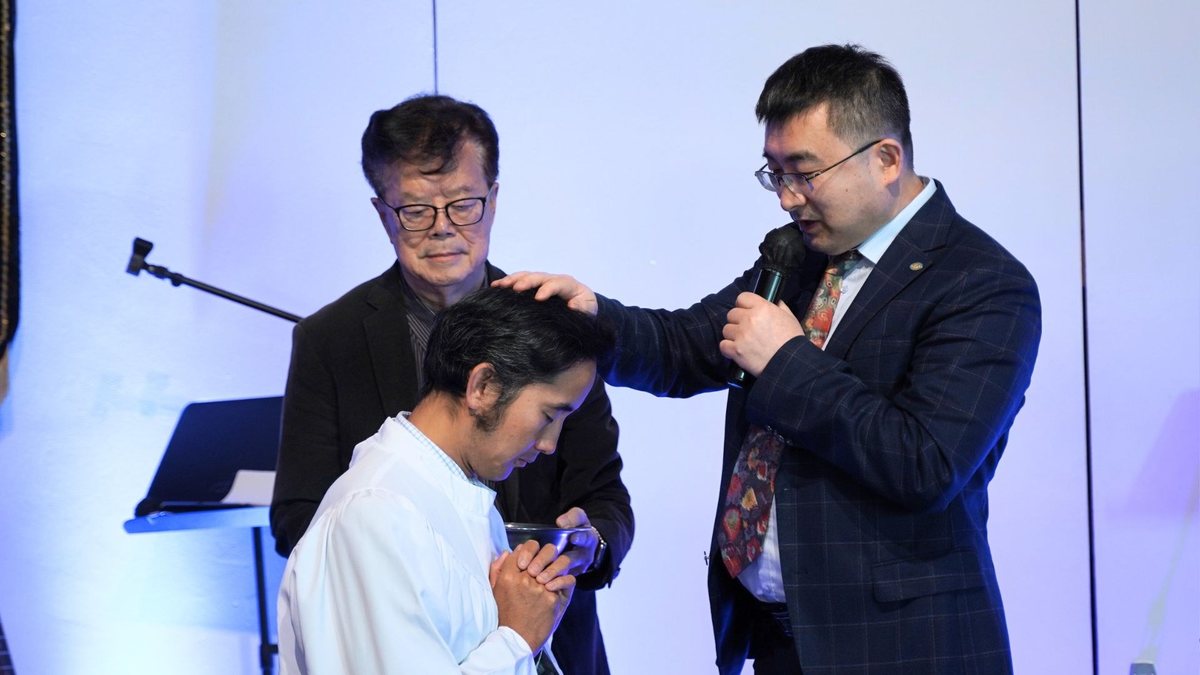 受洗者双手合十低着头,牧师在一旁为他祷告