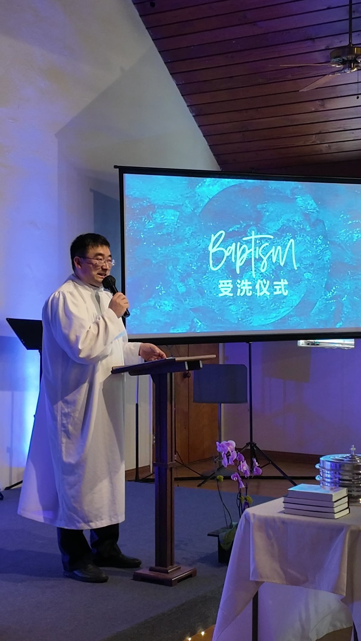 牧师在讲台前主持受洗仪式,屏幕上写着受洗仪式