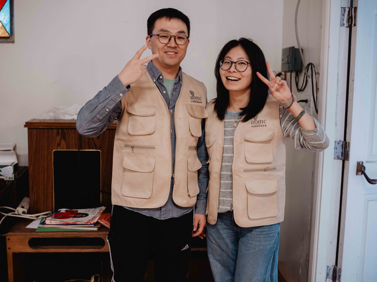两位穿着教会背心的同工在门口比出手势,笑着迎接