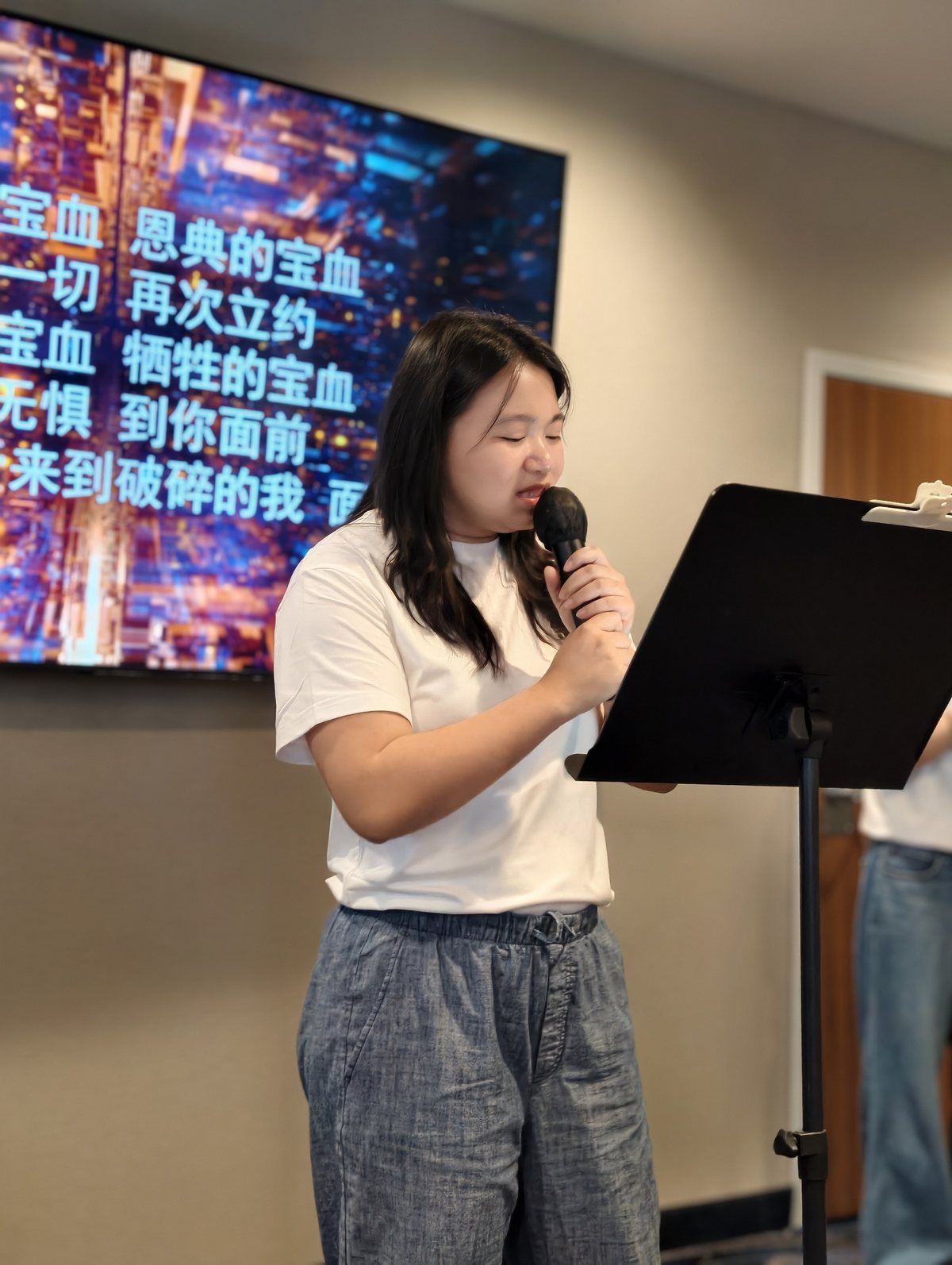 姊妹拿着麦克风唱诗,身后的屏幕打着歌词